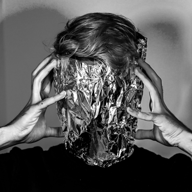 Black and white photo of man holding a large piece of tinfoil over his face.